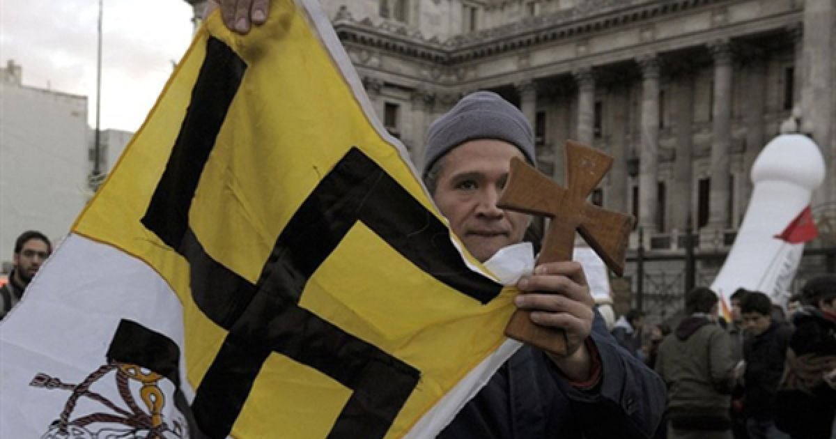 Буенос-Айрес. Чоловік тримає дерев&rsquo;яний хрест та прапор Ватикану із свастикою під час мітингу з вимогою узаконити одностатеві шлюби у Аргентині. Аргентинській сенат збирається дозволити реєструвати між представниками однієї статі. / © AFP