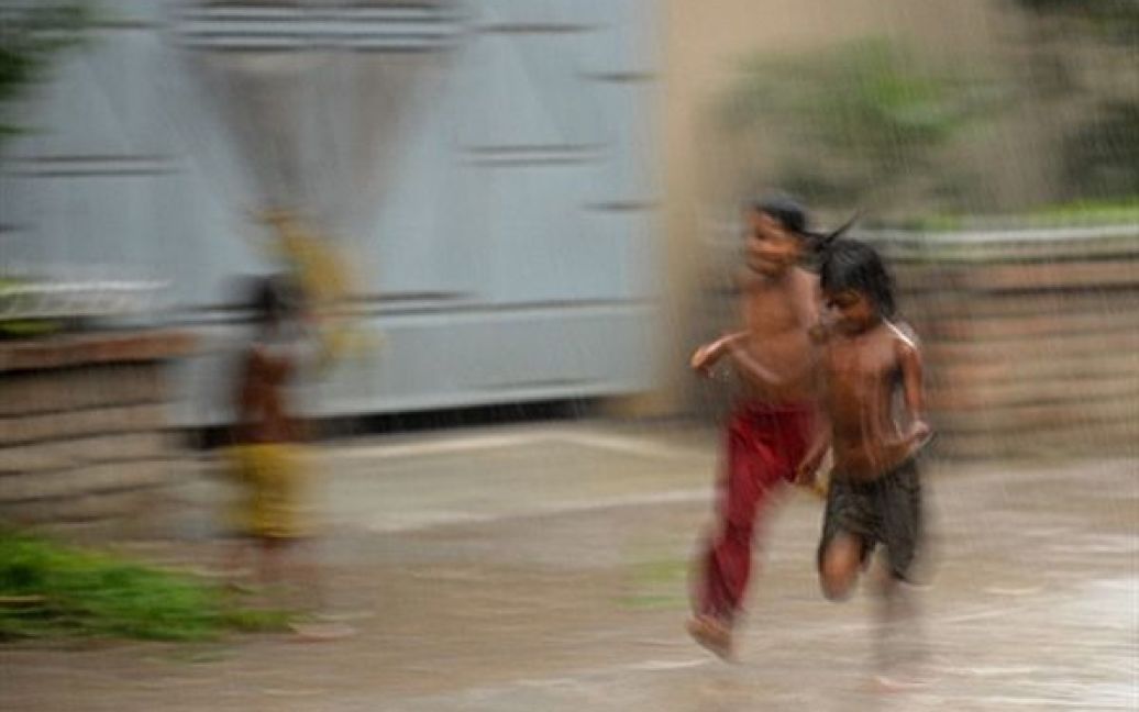 Дакка. Діти біжать під проливним дощем. У Бангладеш розпочався сезон дощів, а з ним і перебої постачання електроенергії, оскільки мережі не можуть витримати напруги. / © AFP