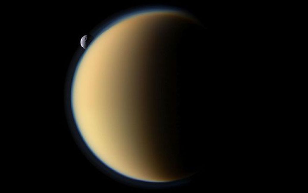 "Кассіні" зробив цю фотографію супутника Сатурна Тефії, на якій видно кратер Одіссей, під час польоту на орбіті Сатурна. Тефія "ховається" за найбільшим супутником Сатурна Титаном. / © 