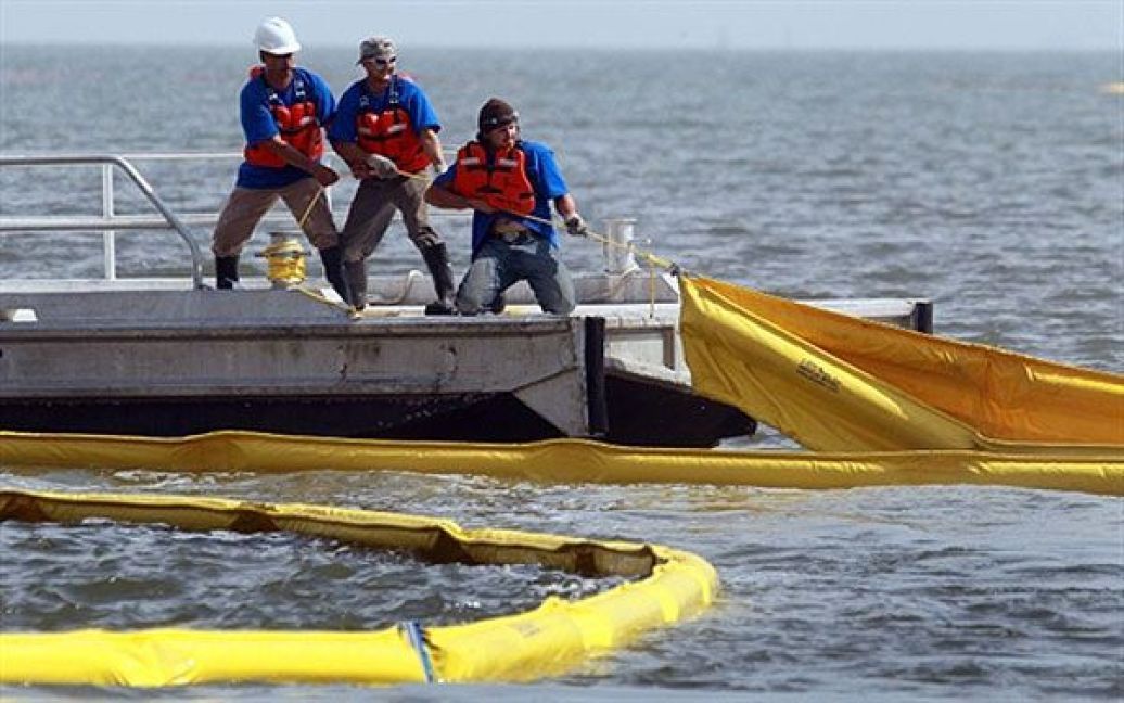 Рятувальники розтягують у воді спеціальні загороджувальні бони, щоб захистити узбережжя від нафти. / © AFP