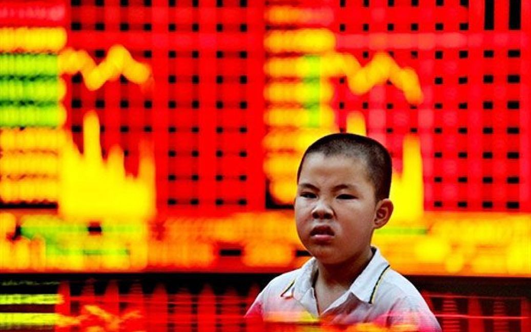 Китай, Шанхай. Китайський хлопчик корчить гримаси перед екранами, що показують фондові індекси на біржі Шанхаю. Центральний банк Китаю встановив найсильніший за кілька років курс обміну для юаня, оскільки міжнародний тиск потребує сильнішої валюти. / © AFP