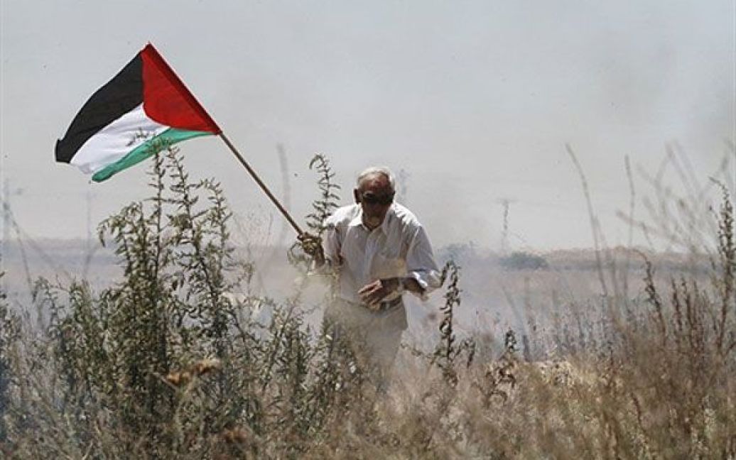 Палестинець тримає національний прапор, доки він біжить до укриття від пострілів ізраїльських військових під час акції протесту на околиці міста Газа. Акція протесту пройшла проти створення Ізраїлем на палестинських землях військової зони, як буферу між прикордонними областями і сектором Газа, який перебуває під контролем "Хамас". / © AFP