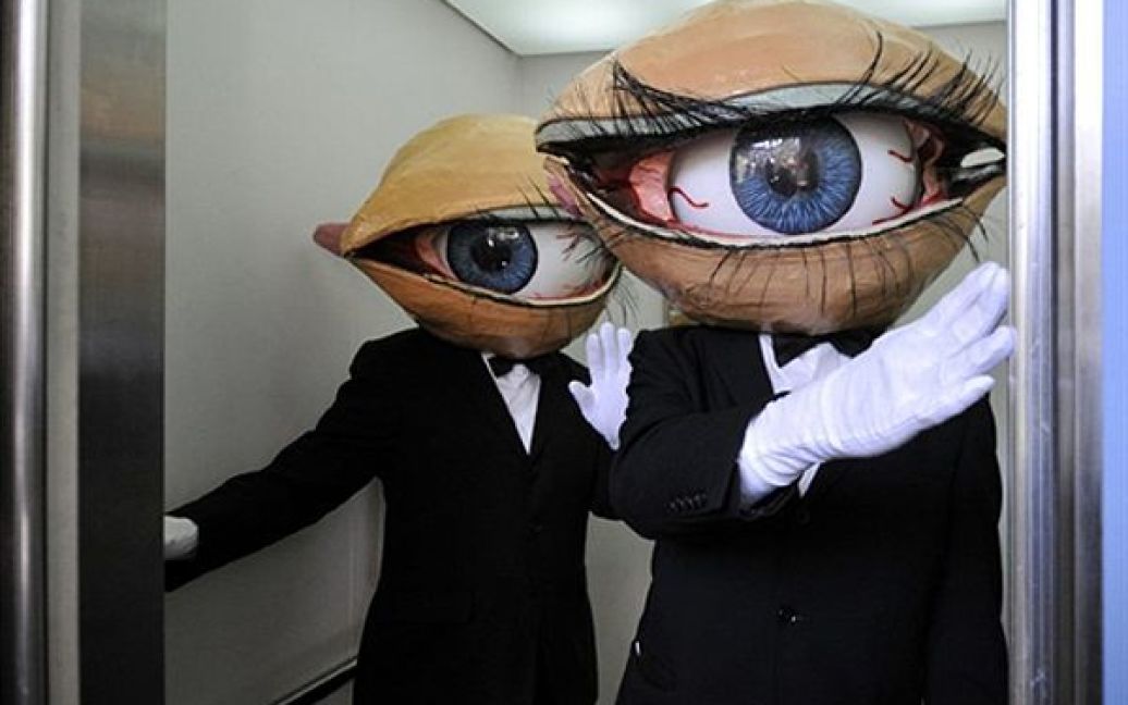Члени трупи Medaman-Medaman, одягнені у маски у вигляді величезних очей, заходять до ліфту Йокогамі. Сотні перехожих змогли насолодитися їх виставою під час фестивалю вуличного театру. / © AFP