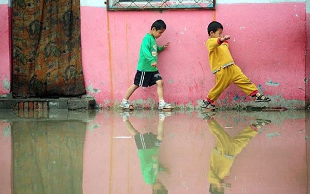 Пекін, Китай. Китайські дітлахи пробігають попід стіною, щоб не впасти у воду. У передмісті Пекіна після сильної зливи затопило кілька вулиць, було закрито школу для дітей робітників-мігрантів. Літні зливи є традиційними для багатьох районів Китаю, щороку через стихію країна зазнає шкоди, часто зливи та повені призводять до сотень жертв. / © AFP