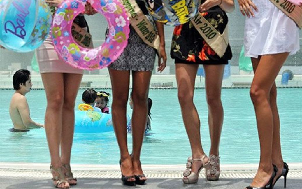 Філіппіни, Маніла. Учасниці конкурсу краси "Міс Земля" позують для фотографів поруч з басейном, в якому купається родина з дитиною. / © AFP