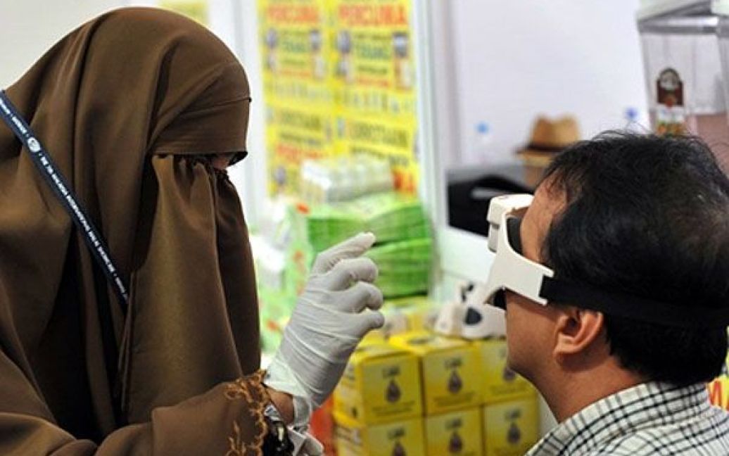 Малайзія, Куала-Лумпур. Закрита мусульманська дівчина демонструє ефективність очних крапель відвідувачу виставки халяльної продукції у Куала-Лумпурі. У Малайзії проходить п&#039;ятиденна міжнародна виставка халяльної продукції. / © AFP