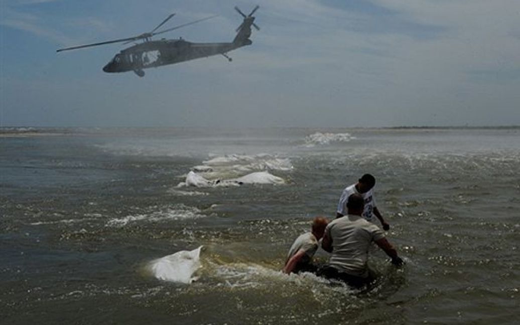 Офіцери берегової охорони штату Луїзіана намагаються збудувати дамбу з мішків з піском, які скидають з гелікоптера, для захисту водних угідь від нафти, яка продовжує виливатися з платформи "Горизонт" компанії ВР. Щодня з платформи "Горизонт", яка вже затонула, виливається більше 5 тонн нафти. / © AFP