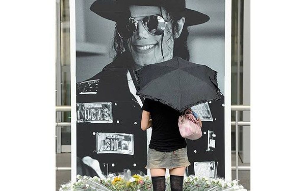 Японія, Токіо. Дівчина стоїть перед великим портретом Майкла Джексона у першу річницю з дня смерті співака. Весь світ згадував Майкла Джексона, який помер у віці 50-ти років. Тисячі прихильників його творчості несли квіти і запалювали свічки на численних меморіалах у різних країнах світу. / © 