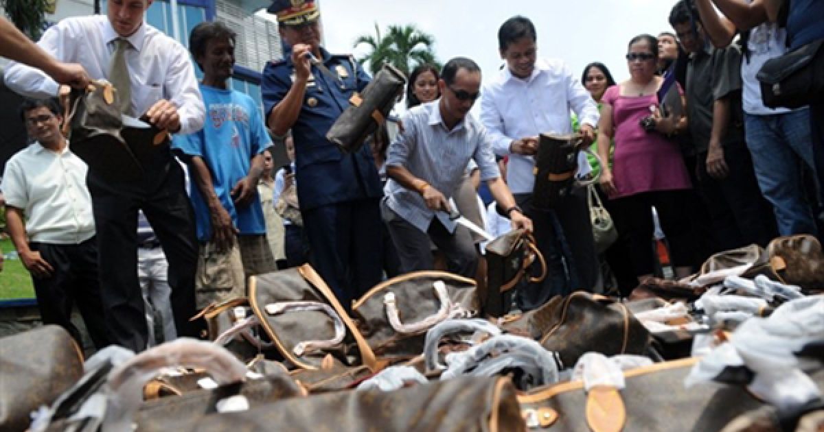 Офіцери філіппінської поліції, співробітники Служби нагляду за використанням інтелектуальних прав та американського посольства знищують контрафактні жіночі сумки перед головним управлінням поліції у Манілі. / © AFP