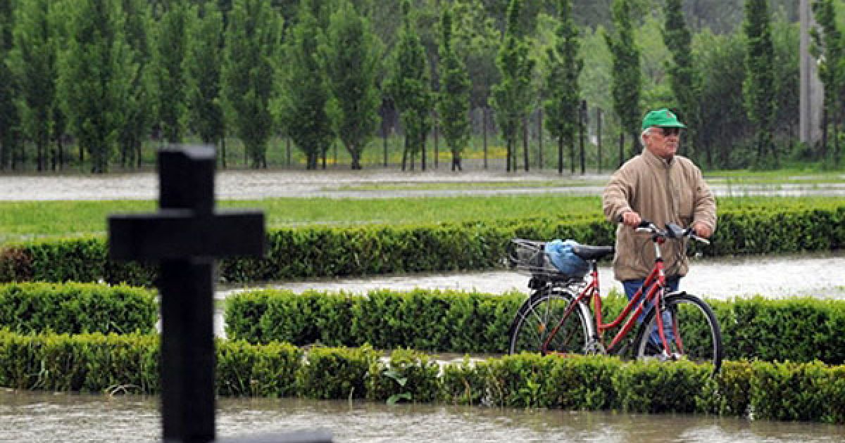Чехія, Богумін. Чоловік штовхає свій велосипед крізь затоплений цвинтар у місті Богумін на сході Чехії. Повені у Центральній Європі призвели до значних руйнувань, було знайдено тіла ще трьох жертв стихії у Польщі та Словаччині, загальне число загиблих в результаті повені досягло дев'яти осіб. Повені також призвели до відключення електроенергії у 3500 будинків у східній частині Чехії. / © AFP