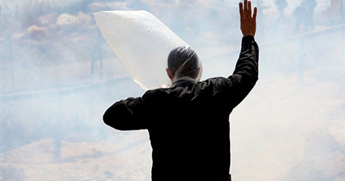 Протестувальник закрився від сльозоточивого газу, який застосувала ізраїльська поліція під час акції протесту у Рамаллі. Посол США Джордж Мітчел закликав міністра оборони Ізраїлю Ехуда Барака до поновлення мирних переговорів з Палестиною. / © AFP