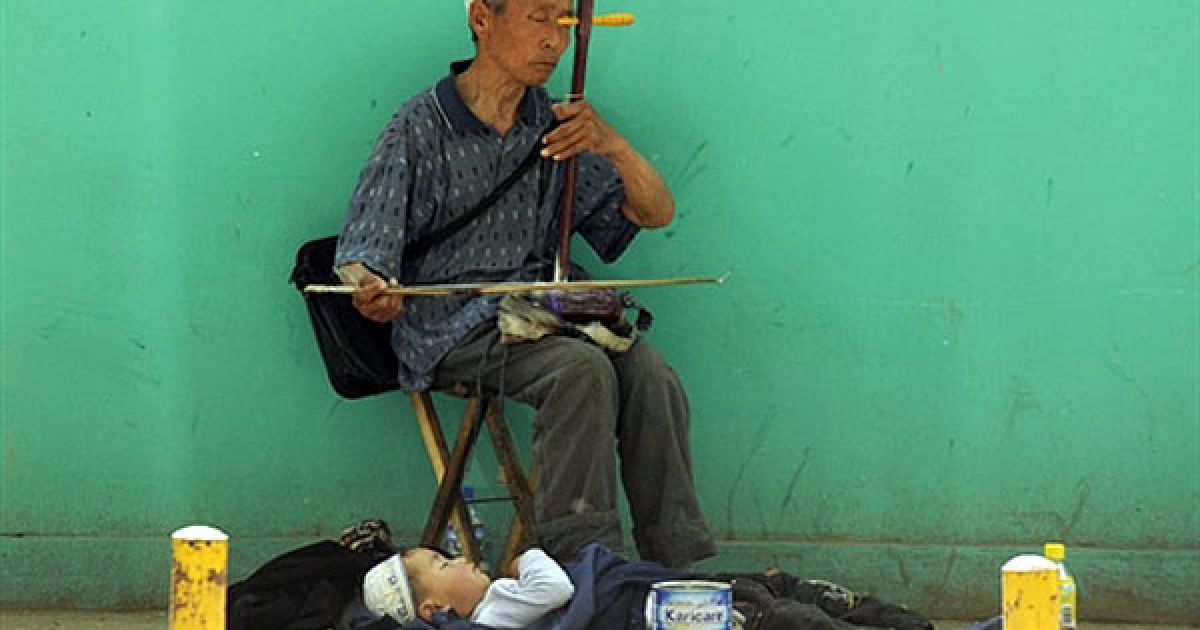 Китай, Пекін. Чоловік грає на ерху, доки його дитина спить біля його ніг на вулиці у Пекіні. Китайський прем&#039;єр-міністр нещодавно заявив, що глобальна фінансова криза виявилася серйознішою і складнішою, ніж очікувалося. Влада закликала населення до активізації співпраці, до прискорення економічного підйому. / © AFP