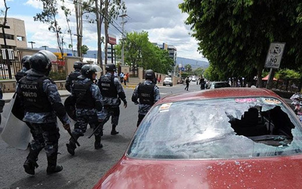 Гондурас, Тегусігальпа. Поліцейські проходять повз автомобіль, розбитий під час акції протесту вчителів у Тегусігальпі. Майже 60 тисяч вчителів страйкують і висловлюють протест проти приватизації системи освіти. / © AFP