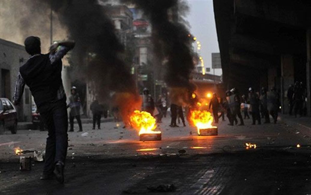 Єгипет, Каїр. Єгипетський ОМОН стоїть поруч із палаючими шинам, доки демонстранти кидають у них каміння під час акції протесту із вимогами повалення президента Хосні Мубарака. / © AFP