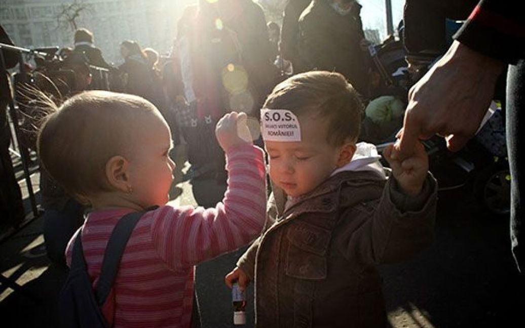 Румунія, Бухарест. Двоє дітей під час акції протесту, яку провели перед штаб-квартирою уряду Румунії у Бухаресті. Мітинг був зібраний матерями, які виступили проти пропозиції Міністерства праці щодо скорочення оплачуваної відпустки з двох років до одного року. На лобі у дитини &ndash; наклейка із написом "SOS &mdash; збережи майбутнє Румунії!" / © AFP