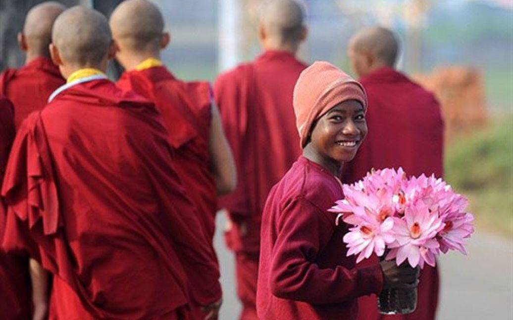Індія, Бодхгайе. Індійський підліток продає квіти лотоса, доки повз нього йдуть буддійські ченці, що прибули на зустріч із Кармапою у Бодхгайе. Близько 5000 буддійських монахів з різних країн світу зібралися у східному індійському місті, щоб взяти участь в урочистостях з нагоди святкування 900-річчя з дня народження першого Кармапи. / © AFP