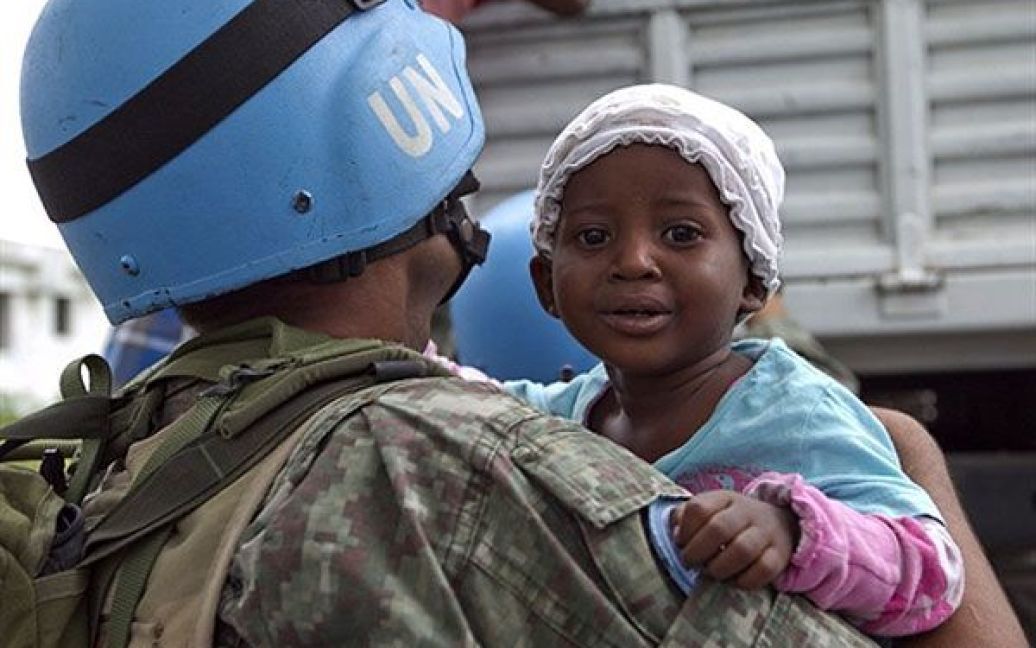 Гаїті, Порт-о-Пренс. Миротворець ООН тримає на руках дитину, доки її матір спускається з вантажівки ООН після прибуття до табору для інтернованих у Порт-о-Пренсі. Місія ООН у Гаїті займається евакуацією населення до більш безпечних місць, оскільки на країну насувається тропічний шторм Томас. / © AFP
