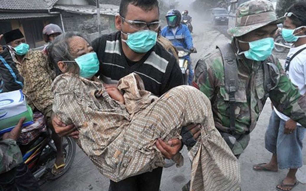 Індонезія, Аргомуліо. Солдат і доброволець допомагають літній жінці у вкритому попелом селищі Аргомуліо на Центральній Яві. В результаті виверження найактивнішого вулкана Індонезії Мерапі, загинули щонайменше 69 осіб. Це виверження стало найбільшим за останні сто років. / © AFP