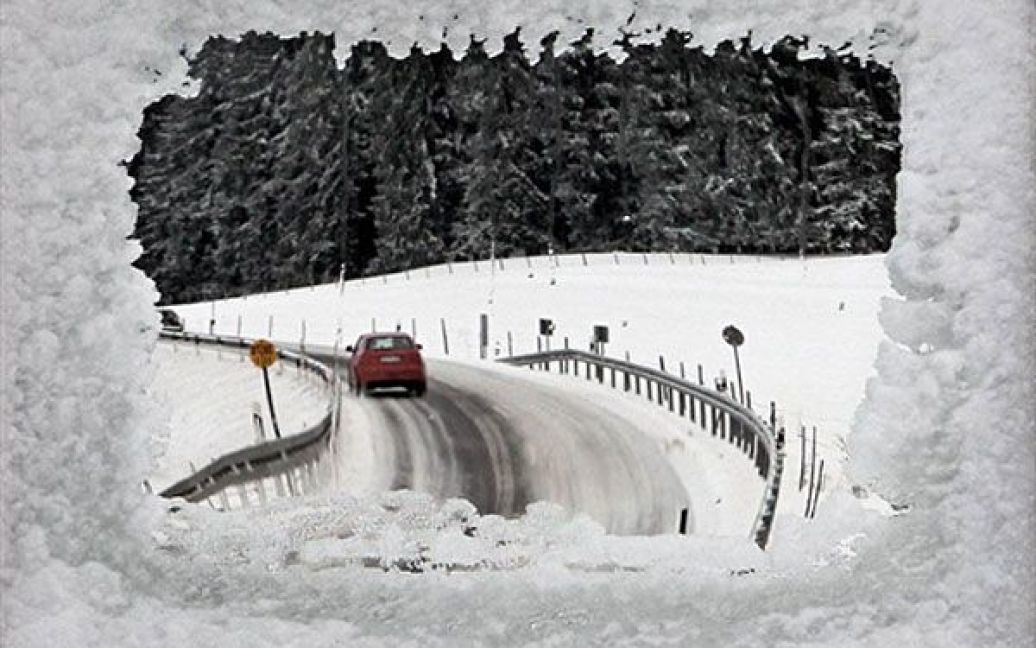 Німеччина, Сіг. Автомобіль, який рухається засніженою дорогою поблизу міста Сіг у південній Німеччині, відбивається у замерзлому дзеркалі безпеки дорожнього руху. У Південній Баварії продовжуються снігопади, а температура утримується на позначці близько нуля. / © AFP