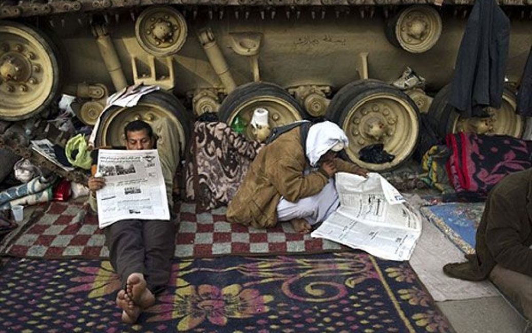 Єгипет, Каїр. Єгипетські антиурядові демонстранти читають свіжі газети, сидячи під БТР-ом на площі Тахрір у центрі Каїра. Тисячі єгипетських демонстрантів продовжують протестувати проти режиму Мубарака. / © AFP
