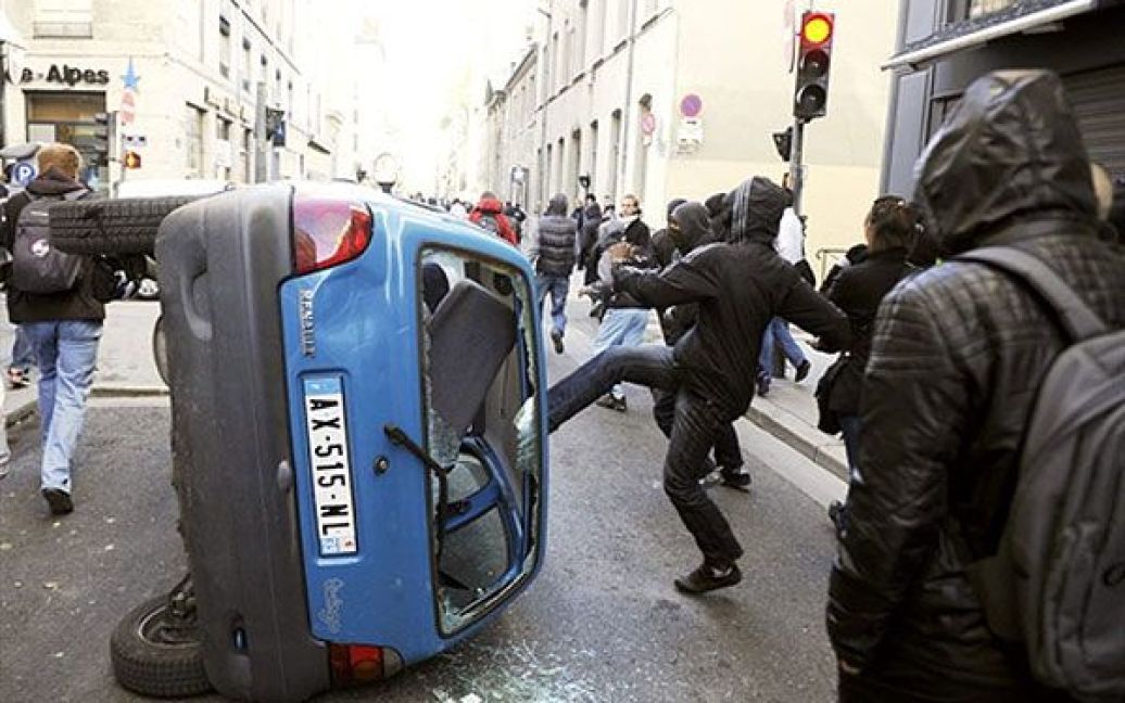 Франція, Ліон. Молодь у масках розбиває автомобіль під час зіткнень демонстрантів з поліцією у місті Ліон на півдні Франції. У Ліоні провели демонстрацію на знак протесту проти пенсійної реформи. / © AFP