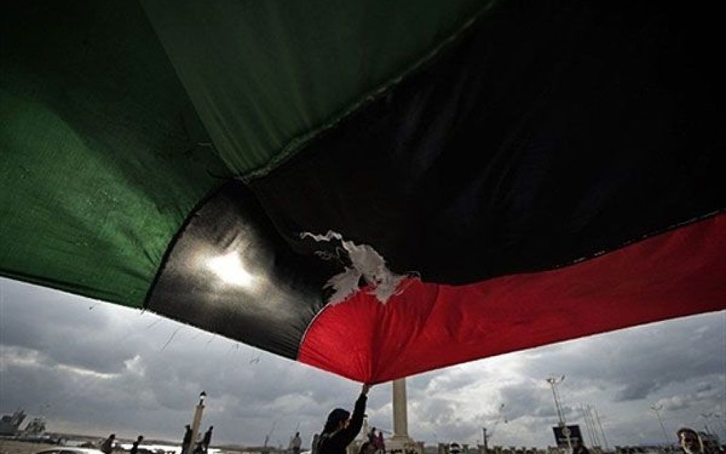 Лівійська Арабська Джамахірія, Бенгазі. Лівієць тримає величезний національний прапор під час багатотисячного мітингу проти режиму Муаммара Каддафі у місті Бенгазі. Лівійських повстанців обстріляли урядові війська, повстанці були змушені відступити до міста Рас Лануф. / © AFP