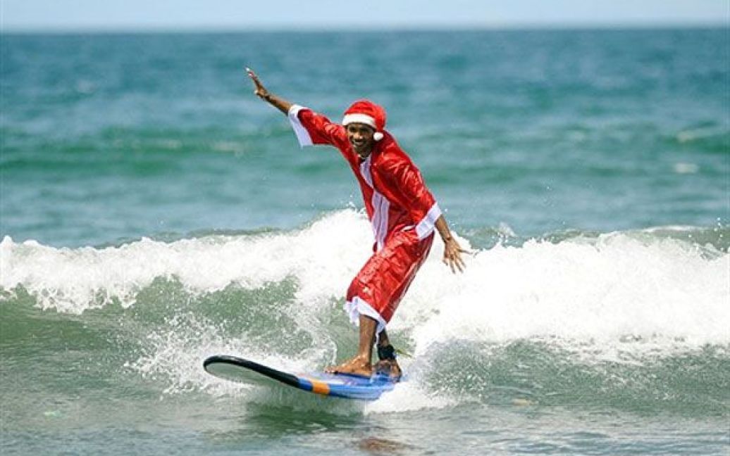 Індонезія, Кута. Серфер, одягнений у костюм Санта Клауса, катається на пляжі Кута на острові Балі. / © AFP