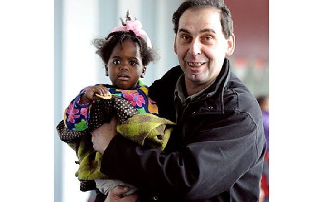 Франція, Руассі-ан-Франс. Французький прийомний батько тримає на руках всиновлену ним дитину з Гаїті. До аеропорту у передмісті Парижа прибув урядовий літак, на якому привезли 114 гаїтянських дітей, яких усиновлять французи. / © AFP