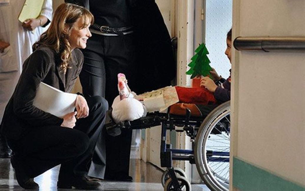Франція, Гарш. Перша леді Франції і всесвітній посол з питань боротьби зі СНІД Карла Бруні-Саркозі розмовляє з дитиною-інвалідом під час візиту до центральної лікарні міста Гарш у передмісті Парижа, куди вона привезла подарунки напередодні Різдва. / © AFP