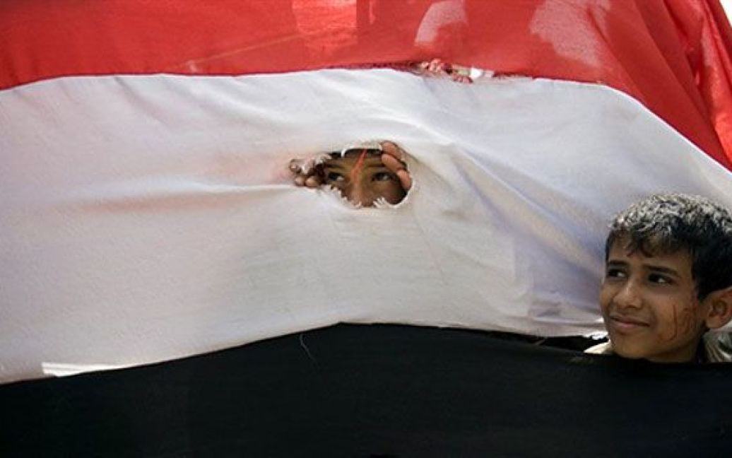 Ємен, Сана. Єменські діти виглядають крізь отвори у національному прапорі під час акції протесту проти режиму президента Алі Абдалли Салеха в Сані. / © AFP