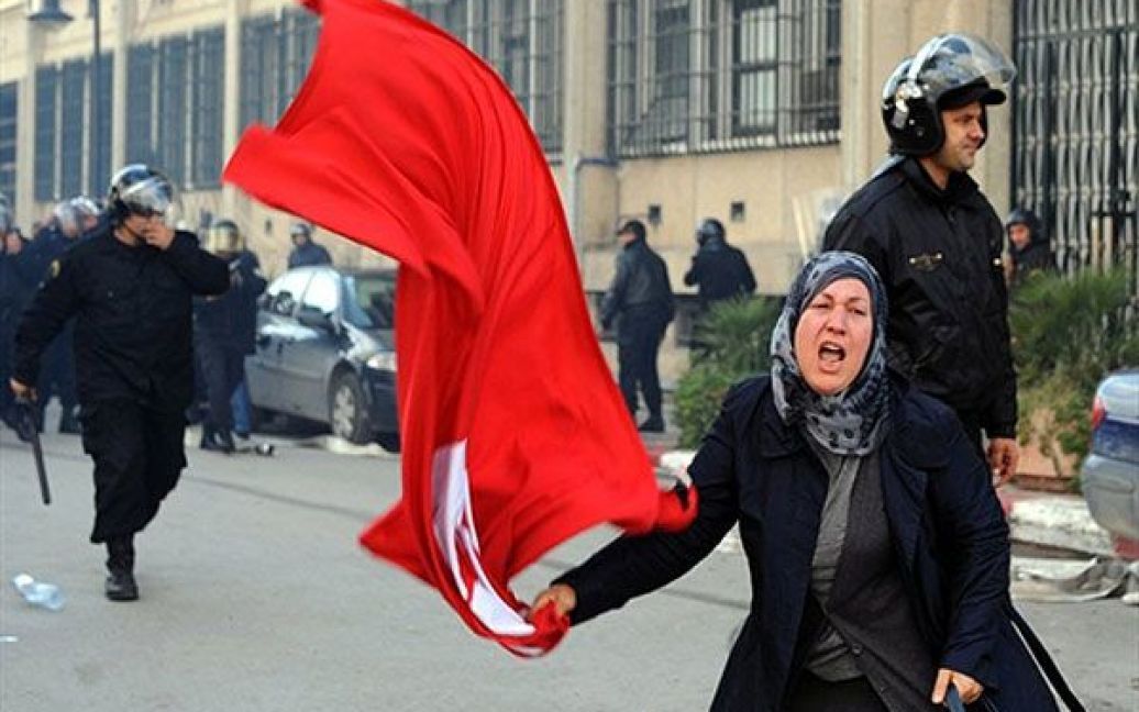 Туніс. Туніська жінка розмахує національним прапором під час зіткнень демонстрантів із силами безпеки на мітингу перед будівлею МВС в Тунісі. Тисячі тунісців вимагали відставки президента країни Зіна аль-Абідіна Бен Алі, в столиці та інших містах відбулись масові акції протесту. / © AFP