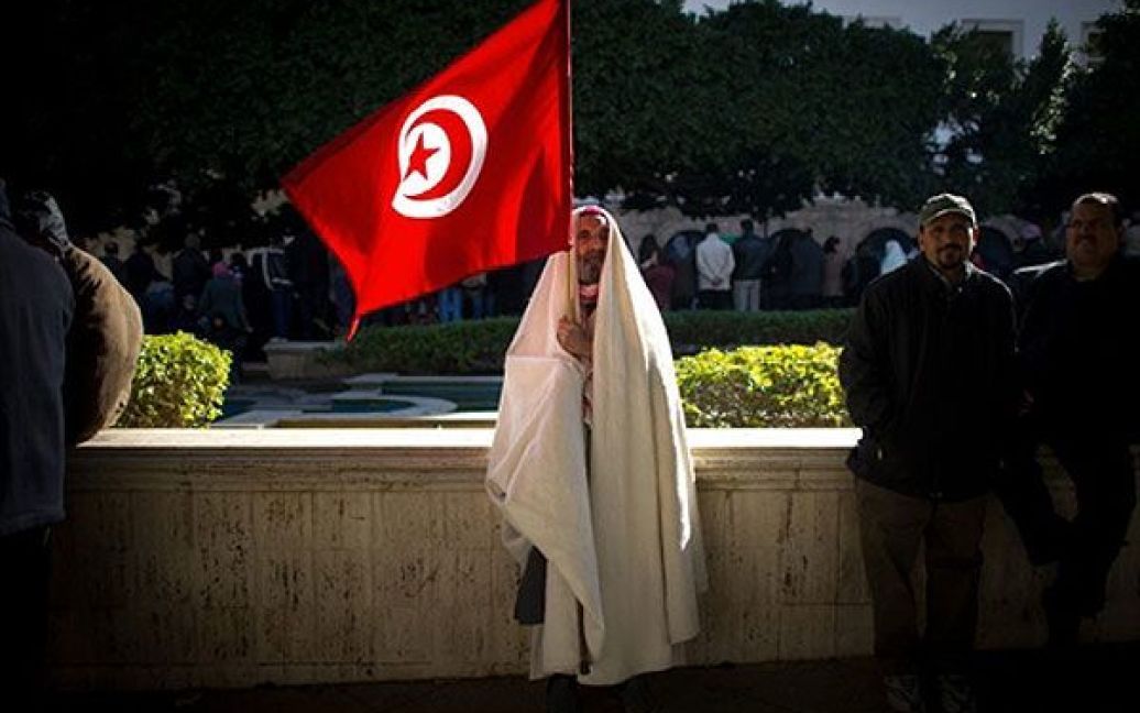 Туніс. Чоловік тримає національний прапор Тунісу під час демонстрації у центрі Тунісу. Тисячі людей зібралися в Тунісі і закликали новий уряд піти у відставку. Прем&#039;єр-міністр країни заяви, що він піде у відставку тільки після того, як в Тунісі відбудуться перші демократичні вибори після здобуття незалежності / © AFP