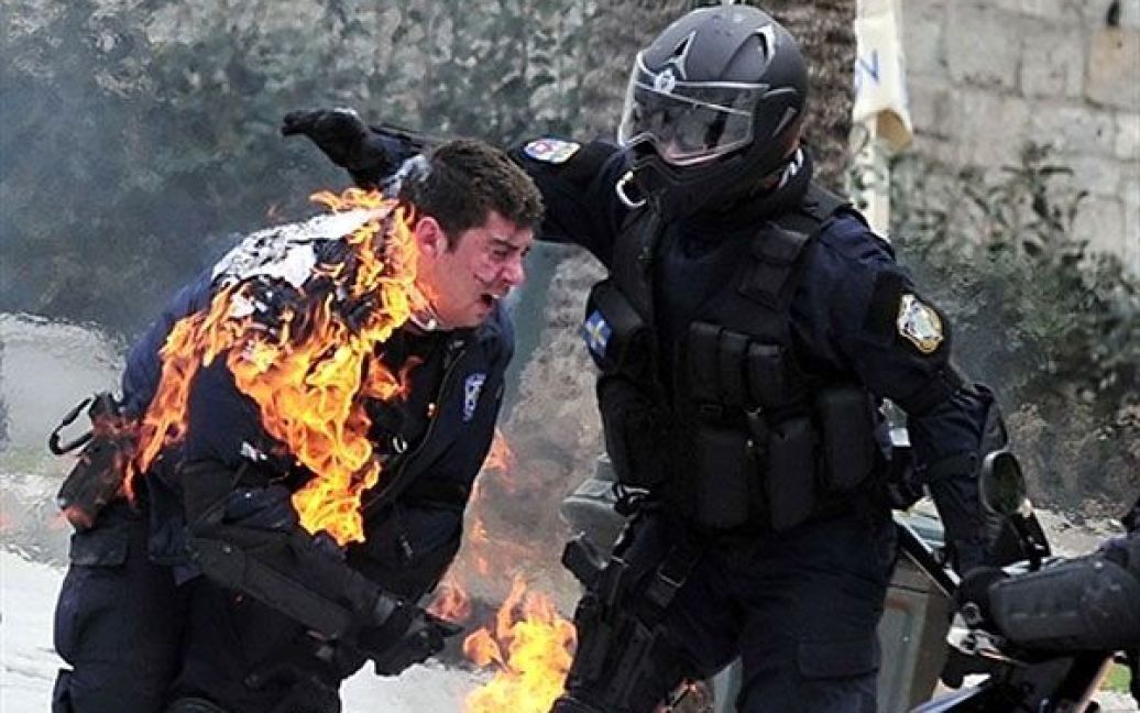 Греція, Афіни. Поліцейському, охопленому вогнем, допомагають його товариші під час зіткнень з демонстрантами у центрі Афін. Поліція застосувала сльозогінний газ поблизу грецького парламенту, коли почалися зіткнення з протестуючими, що кидали у поліцейських каміння і пляшки із запальною сумішшю. / © AFP