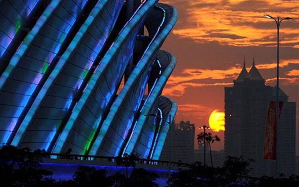 Китай, Гуанчжоу. Сонце сідає за стадіон Haixinsha незадовго до початку урочистої церемонії відкриття 16-их Азіатських ігор в Гуанчжоу. Спортсмени з 45 країн змагатимуться у 42 спортивних дисциплінах. / © AFP