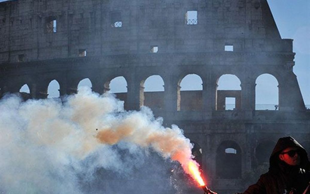 Італія, Рим. Учасник акції протесту за зміну влади тримає фаєр на тлі Колізею. / © AFP