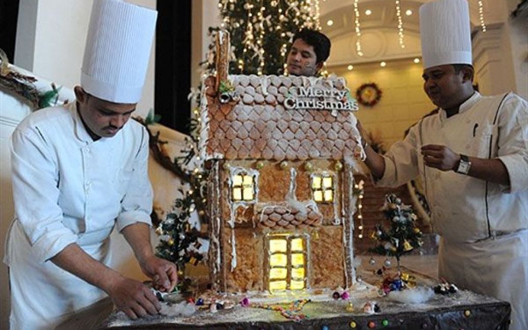 Індія, Ахмедабад. Індійські кухарі додають останні штрихи до "Імбирового будинку", виготовленого напередодні Різдвяних свят у готелі в Ахмедабаді. Цей імбировий будинок, на який використали 700 імбирових печив, троє кухарів готували протягом семи днів. / © AFP