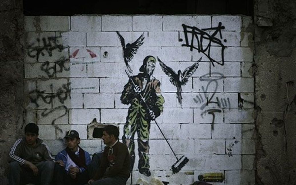 Ліван, Бейрут. Поденні працівники сидять під стіною, на яку нанесено малюнок із зображенням двірника у Бейруті. / © AFP