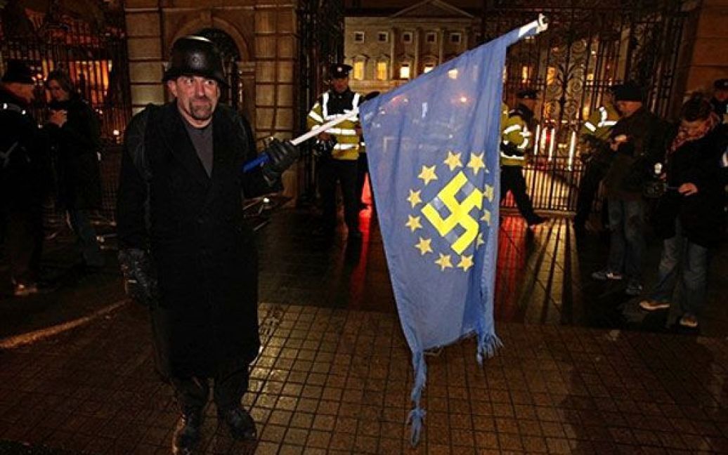 Ірландія, Дублін. Демонстрант тримає прапор ЄС зі свастикою в центрі під час акції протесту перед будівлею ірландського парламенту в Дубліні. Парламент Ірландії проголосував за отримання 85 млрд євро допомоги від ЄС та МВФ. Міністр фінансів Ірландії Браян Леніхан заявив, що це єдиний варіант для відновлення зруйнованої ірландської економіки. / © AFP