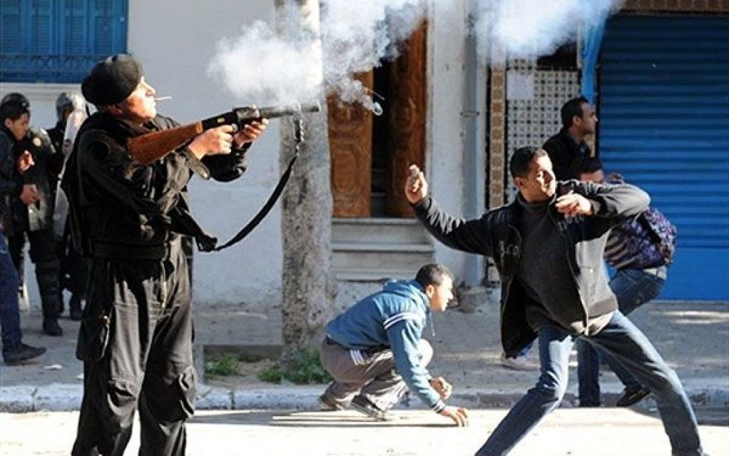 Туніс. Житель Туніса кидає каміння, а поліцейський стріляє сльозоточивим газом у мешканців центрально-туніського регіону Сіді-Бузід під час демонстрації перед офісом прем&#039;єр-міністра Мохаммеда Ганнуші в Тунісі. ОМОН застосував сльозоточивий газ для розгону демонстрантів, що виступили проти тимчасового уряду країни. / © AFP