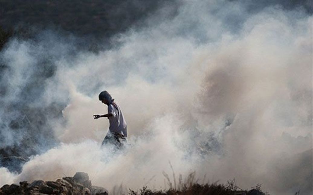 Білин. Палестинець у масці кидає каміння, стоячи у хмарі сльозогінного газу під час зіткнень з ізраїльськими солдатами, які відбулись на щотижневій демонстрації проти розділового бар&#039;єру Ізраїлю у селі Білин поблизу Рамалли. / © AFP