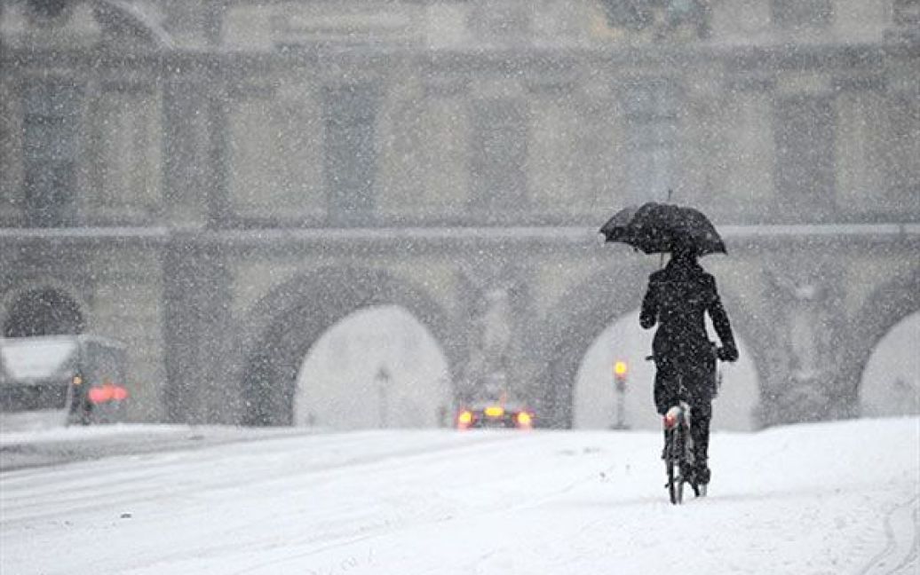 Франція, Париж. Людина їде на велосипеді засніженою вулицею поблизу Лувру. Сильний снігопад вніс свої поправки до Різдвяних канікул у Європі, оскільки призвів до закриття найбільших аеропортів континенту. / © AFP