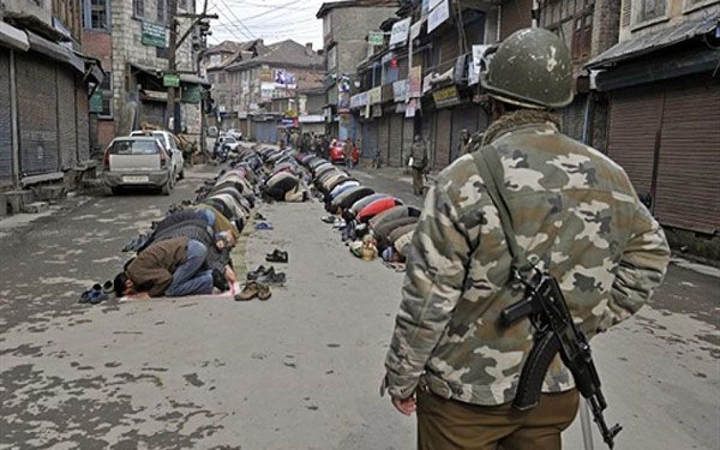 Індія, Срінагар. Кашмірські мусульмани виконують п&#039;ятничну молитву, доки індійський поліцейський дивиться на них. Мусульмани організували страйк, щоб відзначити 27-му річницю смерті засновника Фронту звільнення Джамму і Кашмір Макбула Бхата. / © AFP