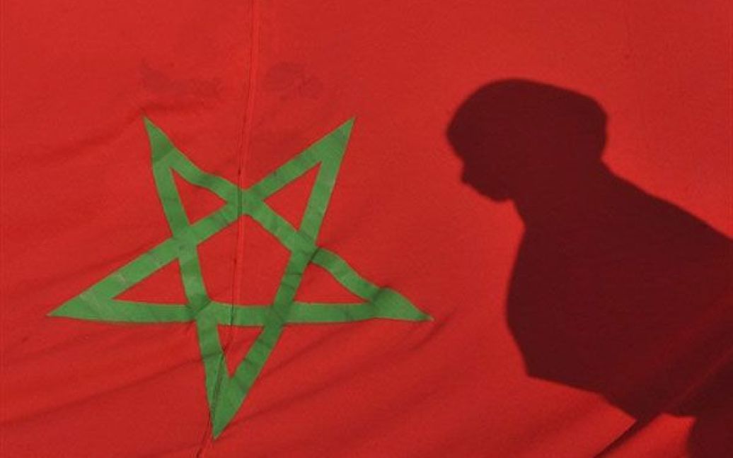 Марокко, Рабат. Тінь молодої жінки відбивається на марокканському прапорі під час демонстрації у Рабаті, яку провели на честь 35-річчя "Зеленого маршу". У листопаді 1975 року марокканський король Хасан II закликав 350 тисяч марокканців, "озброєних" Кораном і національними прапорами, вирушити до кордону із Західною Сахарою, щоб підтримати незалежність колишньої іспанської колонії. Колишня іспанська колонія, Західна Сахара, була анексована Марокко у 1975 році. / © AFP