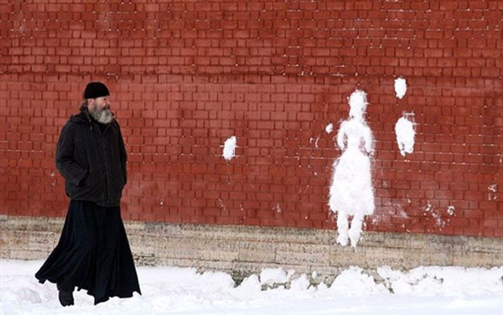 Росія, Санкт-Петербург. Священик РПЦ дивиться на силует зі снігу на стіні Санкт-Петропавлівської фортеці у центрі Санкт-Петербурга. У Санкт-Петербурзі знову почались снігопади і температура впала нижче 0 градусів за Цельсієм. / © AFP