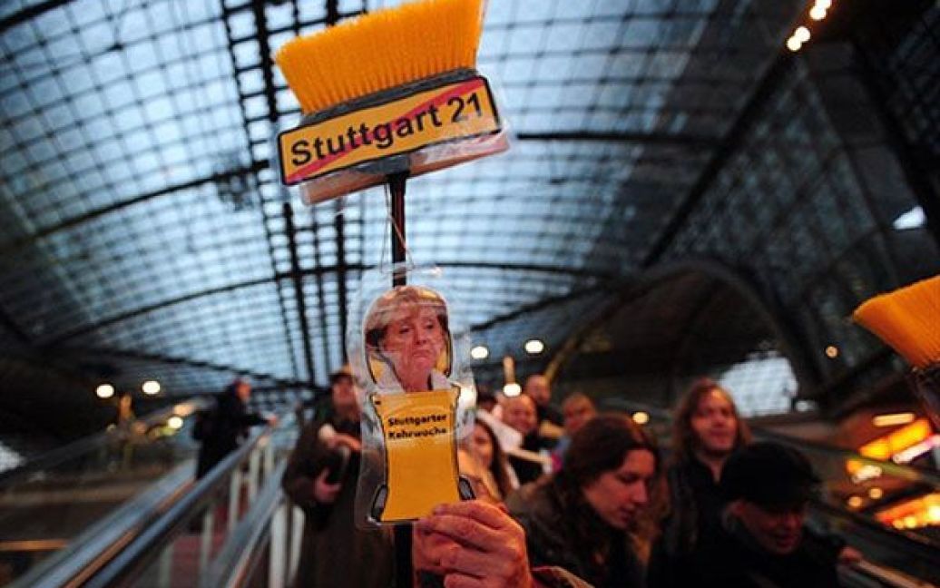 Німеччина, Берлін. Протестуючі тримають мітлу, прикрашену портретом федерального канцлера Німеччини Ангели Меркель і написом "Ні Штуттгарт 21", під час акції протесту проти початку проекту "Залізниця Штуттгарт 21". Близько 600 демонстрантів зібрались на акцію протесту біля головного залізничного вокзалу в Берліні. / © AFP