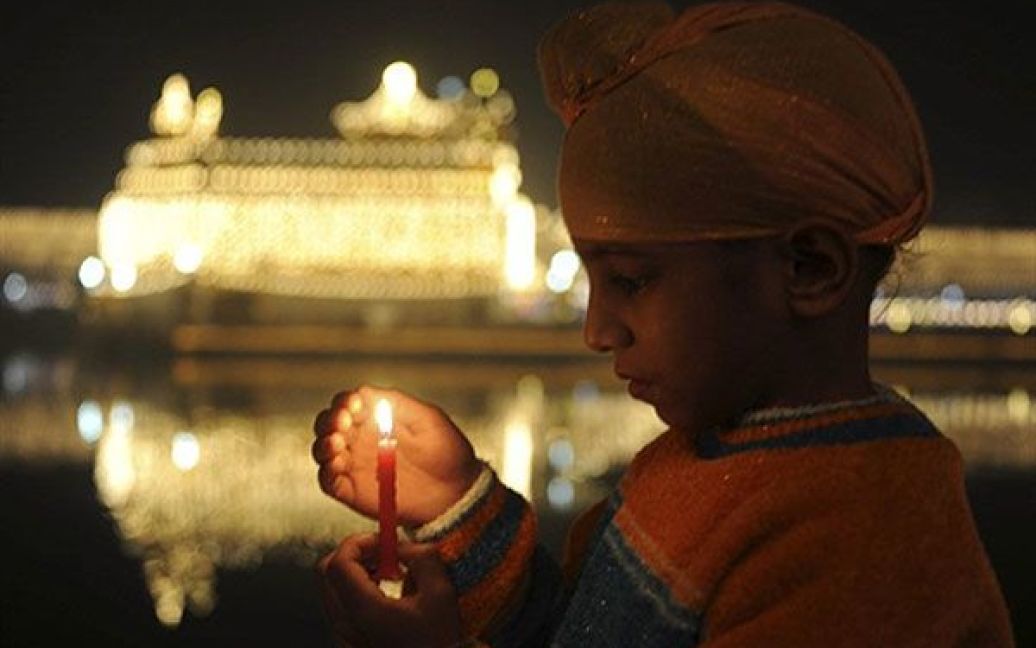 Індія, Амрітсар. Індійський хлопчик-сикх тримає свічку під час церемонії вшанування перед Золотим Храмом у Амрітсарі. / © AFP