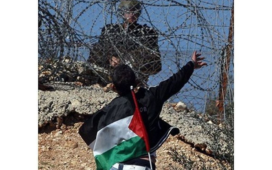 Білин. Палестинський демонстрант кидає камінь у напрямку ізраїльського солдата, що стоїть на іншій стороні розділового бар&rsquo;єру Ізраїлю. / © AFP
