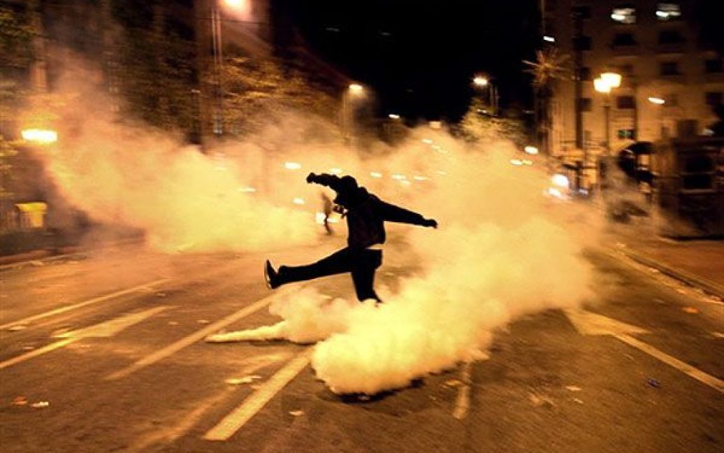 Греція, Афіни. Демонстрант штовхає ногою балончик зі сльозогінним газом у центрі Афін під час безладів, що спалахнуди у столиці Греції напередодні другої річниці вбивства 15-річного хлопчика, який був застрелений поліцією. Близько 100 молодиків кидали каміння у вікна банків та магазинів, підпалювали сміттєві баки. / © AFP