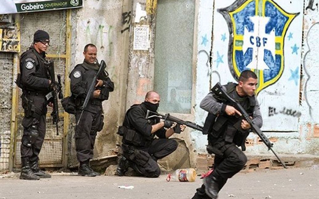 Бразилія, Ріо-де-Жанейро. Співробітник поліцейського спецпідрозділу рушає вперед, доки інші стоять біля входу до району нетрів Віла Крузейро у Ріо-де-Жанейро. Наркоторговці здійснили кілька нападів на поліцейські машини та підпалили їх у відповідь на проведення поліцейських операцій у деяких нетрях міста. Щонайменше 23 людини було вбито і 153 заарештовано протягом кількох днів зіткнень бразильських сил безпеки і банд наркоторговців. / © AFP