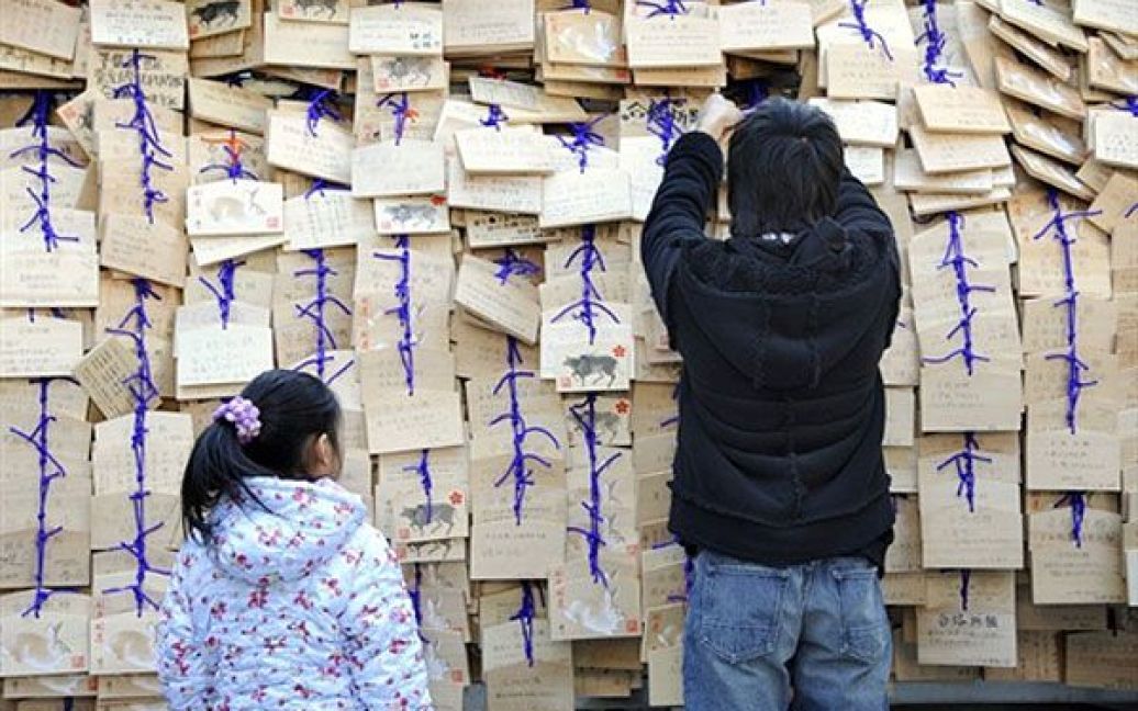 Японія, Токіо. Дівчина і хлопець розвішують дерев&#039;яні таблички з обітницями і своїми побажаннями у храмі Юсіма Тендзін в Токіо. Учні та їх батьки приходять до синтоїстських і буддійських храмів по всій Японії, щоб помолитися за успіх на вступних шкільних іспитах. / © AFP
